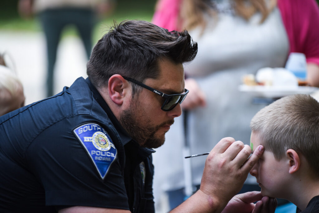An officer uses facepaint on a child at a cookout.