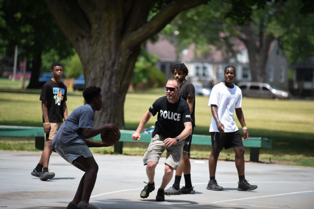 An officer plays basketball with children at a park.